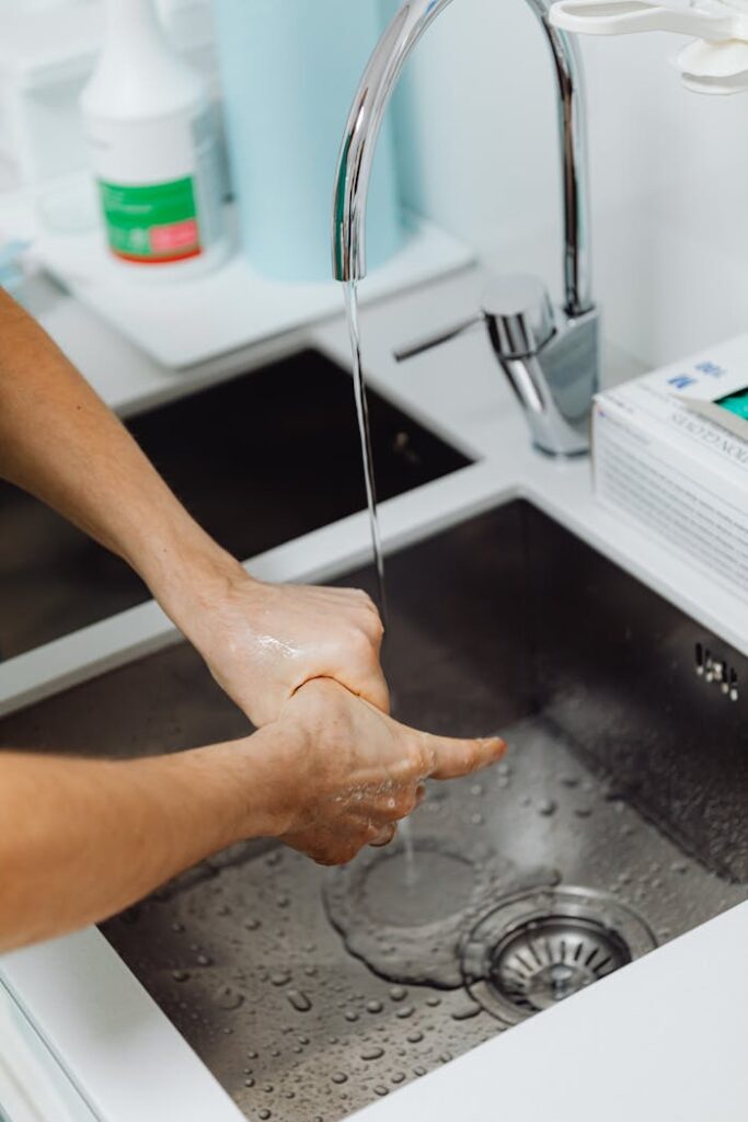 Hands being washed under running water in a modern stainless steel sink, promoting hygiene.